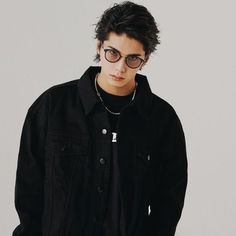 a young man wearing glasses standing in front of a white wall