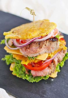 a large sandwich with meat, cheese and vegetables on it sitting on top of a cutting board