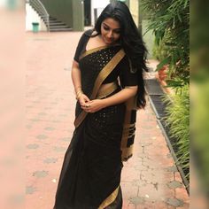 a woman in a black and gold sari is walking down the street with her hand on her hip