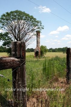 an old wooden fence in the middle of a field with a brick chimney behind it