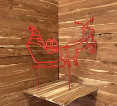 a wooden wall with a red metal reindeer on it's side and a wood bench in front of it