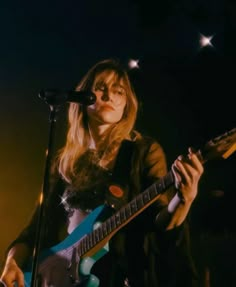 a woman holding a guitar while standing in front of a microphone