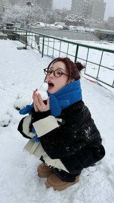 a woman kneeling down in the snow with her mouth open and holding something up to her face