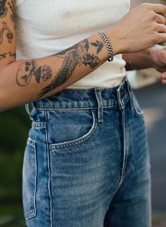 a man with tattoos on his arm and wrist is looking at his cell phone while wearing jeans