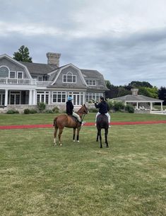 two people riding horses in front of a large house