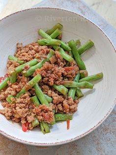 a white bowl filled with green beans and meat