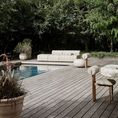 a wooden deck next to a pool with chairs and tables on top of it, surrounded by greenery