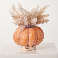 a small pumpkin shaped planter with white flowers in it's center sits on a table