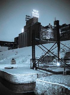 a black and white photo of an industrial area with buildings in the background at night