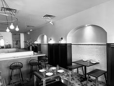 a black and white photo of a restaurant with tables, stools, and an oven