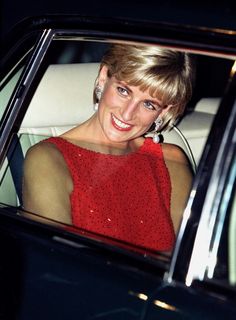 a woman sitting in the back seat of a car wearing a red dress and smiling