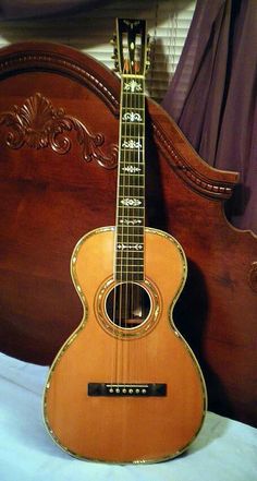 an acoustic guitar sitting on top of a bed next to a wooden headboard and foot board