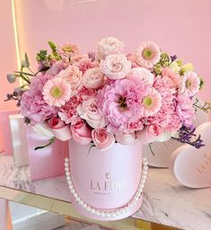 a pink flower box with flowers in it on top of a table next to a mirror