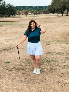 a woman in a blue shirt and white skirt is holding a golf club while posing for the camera