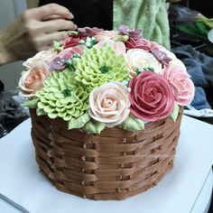 a cake decorated with flowers on top of a white tableclothed surface next to a woman's hand