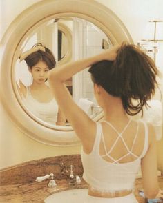 a woman sitting in front of a mirror brushing her hair