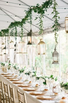 a long table is set with place settings and hanging lanterns