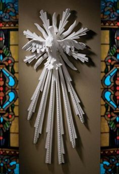 a clock made out of white paper sitting on top of a wall next to a stained glass window