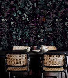 two chairs sitting at a table in front of a wall with flowers and plants on it