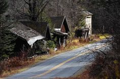 an old run down road with abandoned buildings on the side and trees in the background