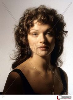 a woman with long curly hair posing for a photo in front of a white background