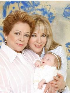 two women are holding a baby in their arms and posing for a photo with blue flowers on the wall behind them