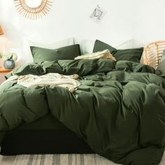 an unmade bed in a white room with green sheets and pillows on the floor