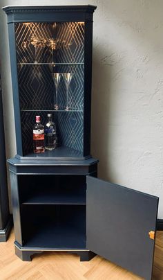 a black cabinet with two glasses on top and a liquor bottle in the bottom shelf