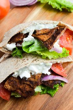 two pita sandwiches with lettuce, tomatoes and onions on a cutting board