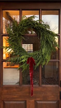 a wreath hanging on the front door of a house with a red ribbon tied around it