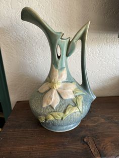 a vase with flowers painted on it sitting on a wooden table next to a wall