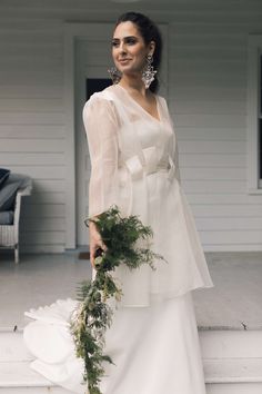 a woman in a white dress is standing on the steps with greenery around her