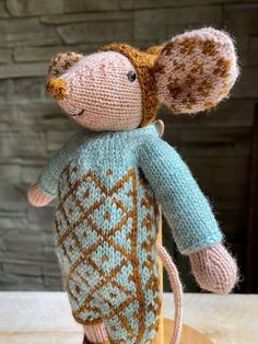 a knitted mouse is sitting on top of a wooden stand and wearing a sweater