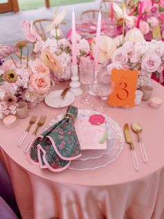 the table is set with pink and white flowers, napkins, silverware, and candles