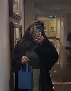 a woman taking a selfie with her cell phone in front of her face while holding a blue purse