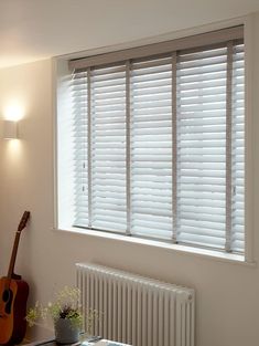 a white room with a guitar on the table and window blinds in front of it