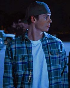 a young man wearing a plaid shirt and black hat standing in the street at night