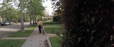 a woman walking down a sidewalk next to trees