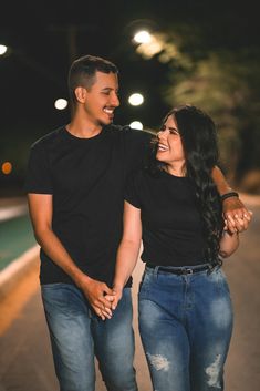 a man and woman are walking down the street at night with their arms around each other