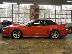 an orange sports car parked in a garage next to large windows with american flag on it