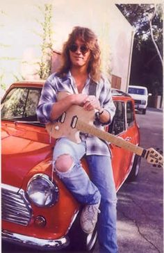 a man sitting on top of an orange car holding a guitar