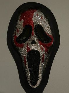 a black mask with red and white designs on it's face is hanging from the wall