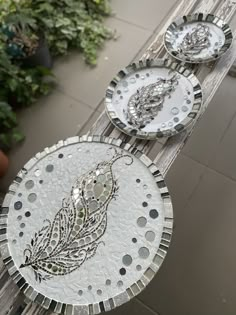 three decorative glass plates sitting on top of a wooden table next to potted plants