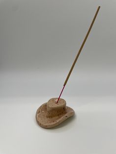 a small wooden hat with a stick sticking out of it's side on a white surface