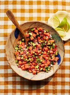 a bowl filled with chopped vegetables on top of a checkered table cloth next to a wooden spoon