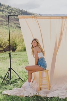 a woman is sitting on a stool in front of a photo shoot with a backdrop