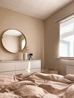 a bedroom with a bed, dresser and round mirror on the wall above it's headboard