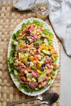 a salad with meat, lettuce and olives on a white platter