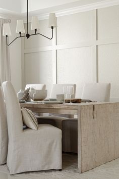 a dining room table with two chairs and a bench in front of it, next to a white wall