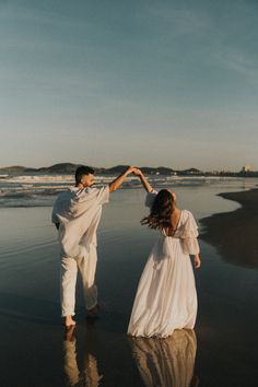 a man and woman holding hands while walking on the beach